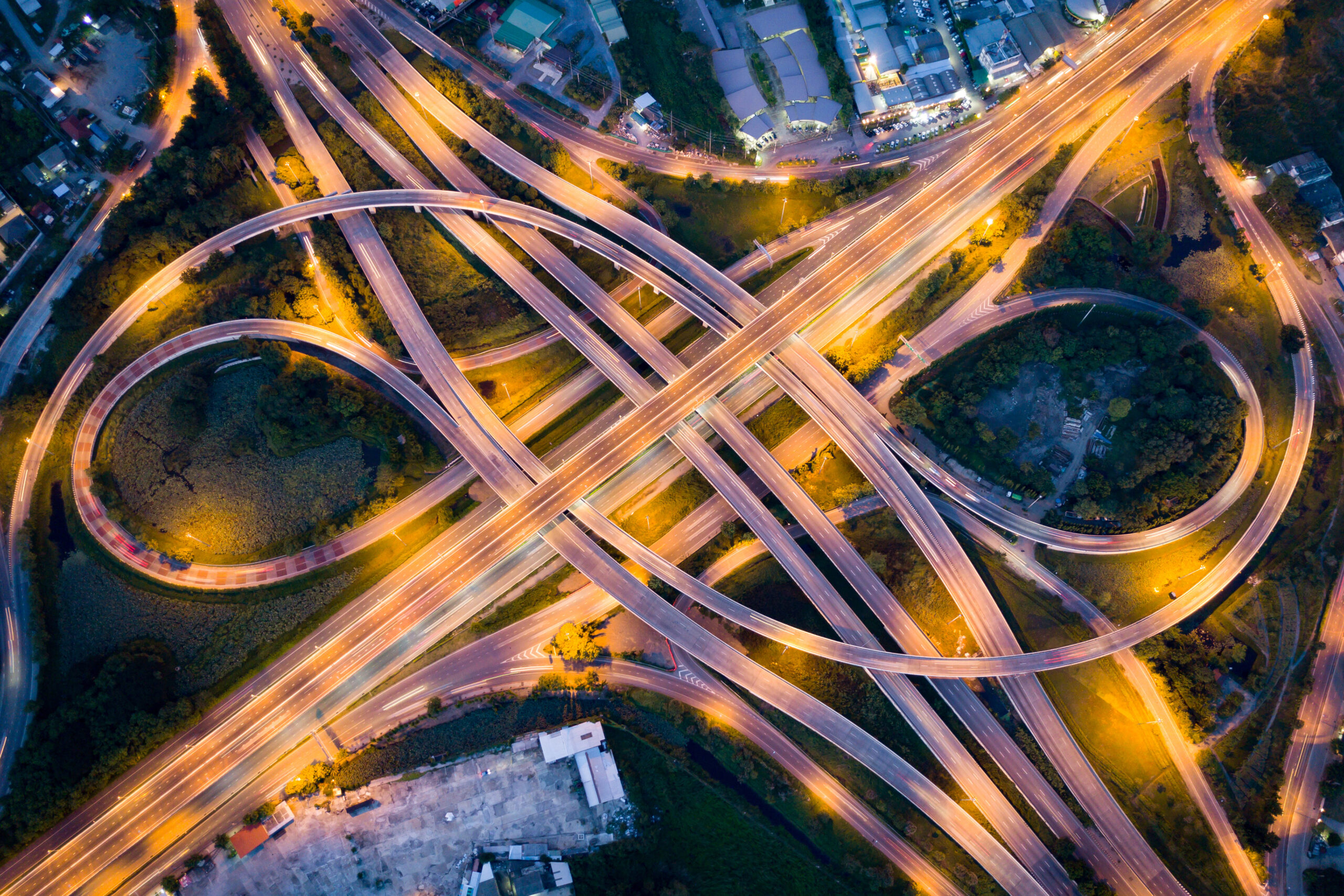 Aerial view of illuminated road interchange or highway intersection with busy urban traffic speeding on the road at night.