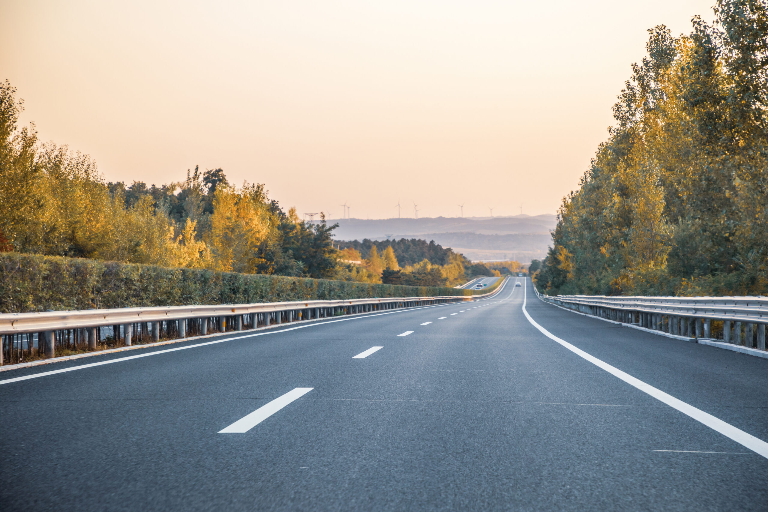 The highway that goes through the autumn forest and in the distance you can see cars and hills with windmills in the background