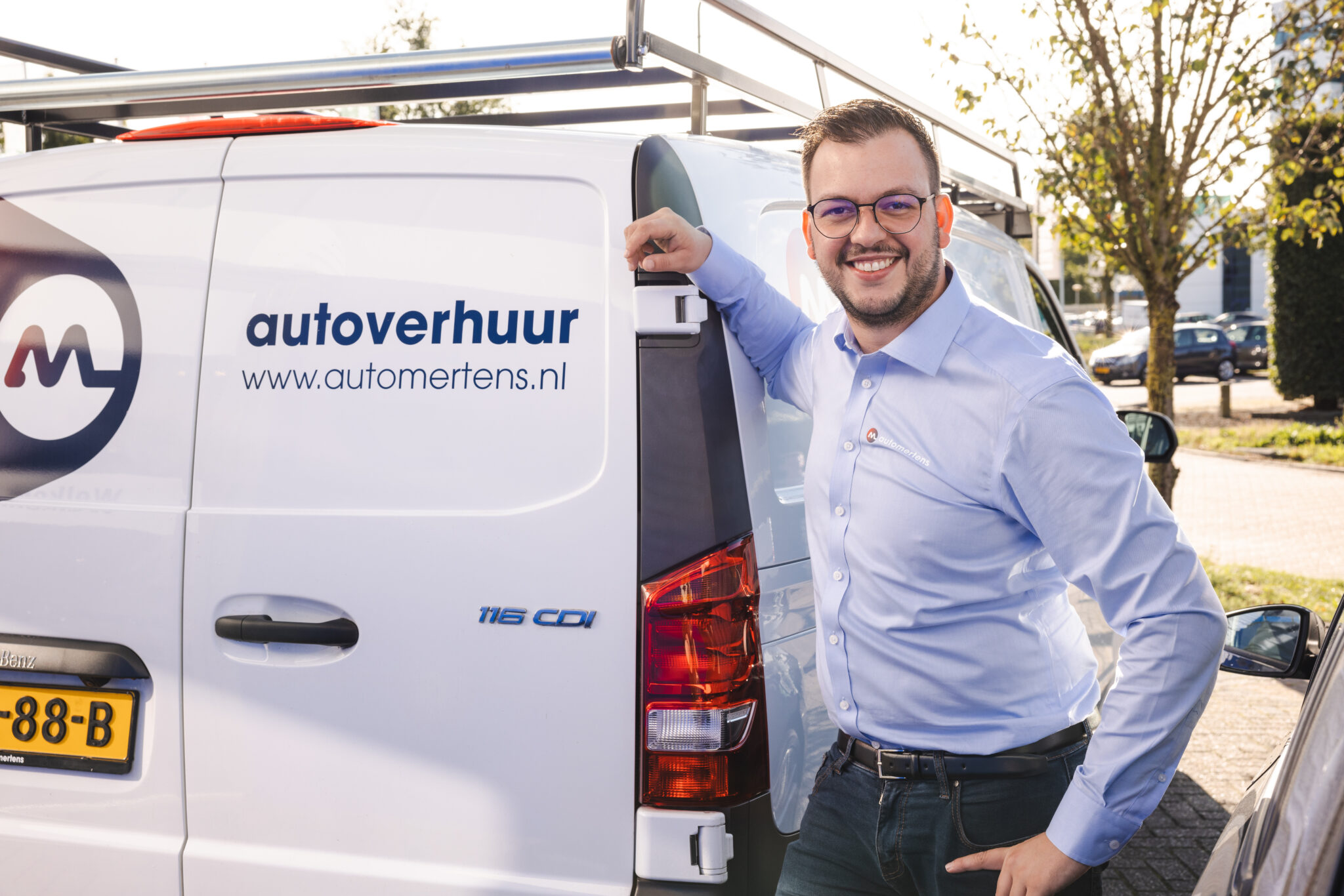 A man stands leaning against an Autoverhuur automobile